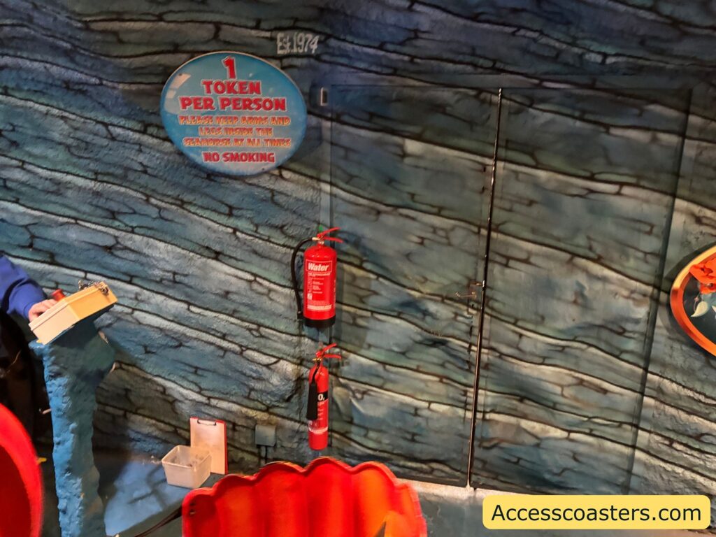 Themed interior of the Neptune’s Kingdom ride, showing walls designed to look like underwater planks, a red ride vehicle, and a visible fire extinguisher.