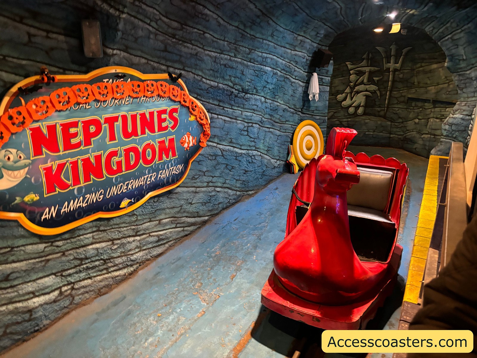 The loading area for Neptune’s Kingdom, featuring a red ride vehicle and a large themed sign that reads “Neptune’s Kingdom: An Amazing Underwater Adventure.”