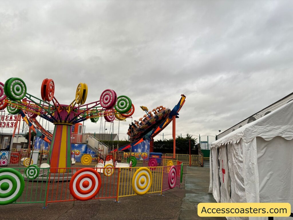 he Disko ride in motion, featuring a colorful spinning platform with outward-facing seats set on a curved track, enclosed by yellow railings