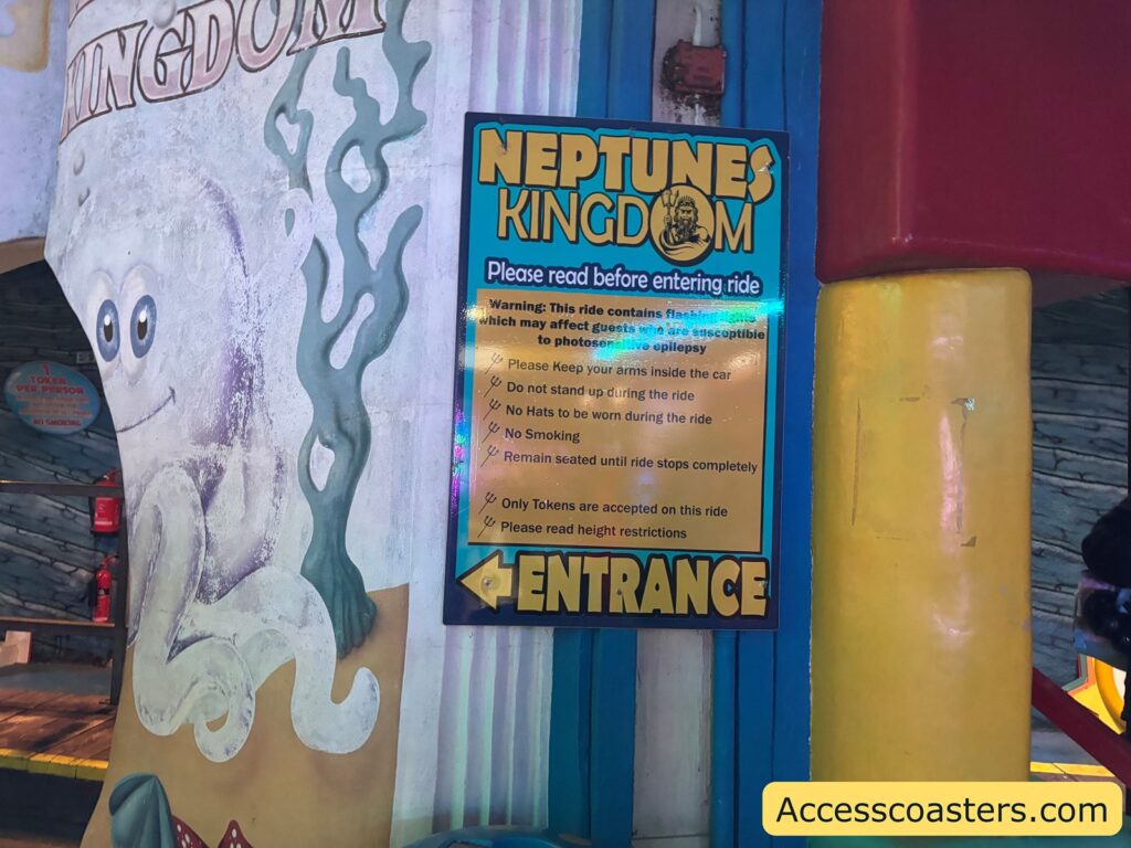 Close-up view of the Neptune’s Kingdom entrance sign, with a yellow information board about ride access and entrance details.