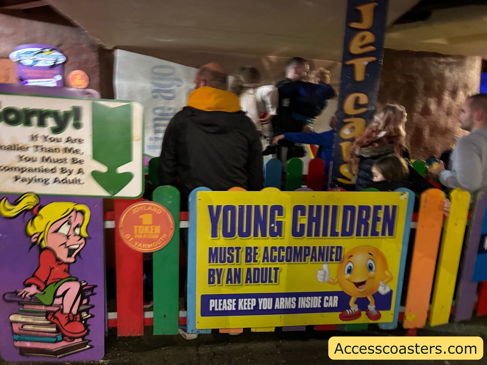 Ride entrance showing a sign stating "Young Children Must Be Accompanied By An Adult," with people waiting and part of the jet cars visible.