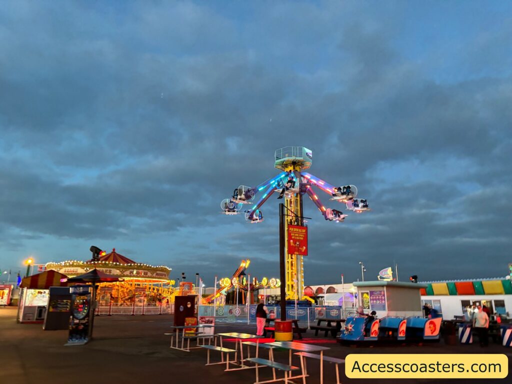 Distant view of Lightning 360 spinning rides and surrounding fairground, with food stalls and benches in the background