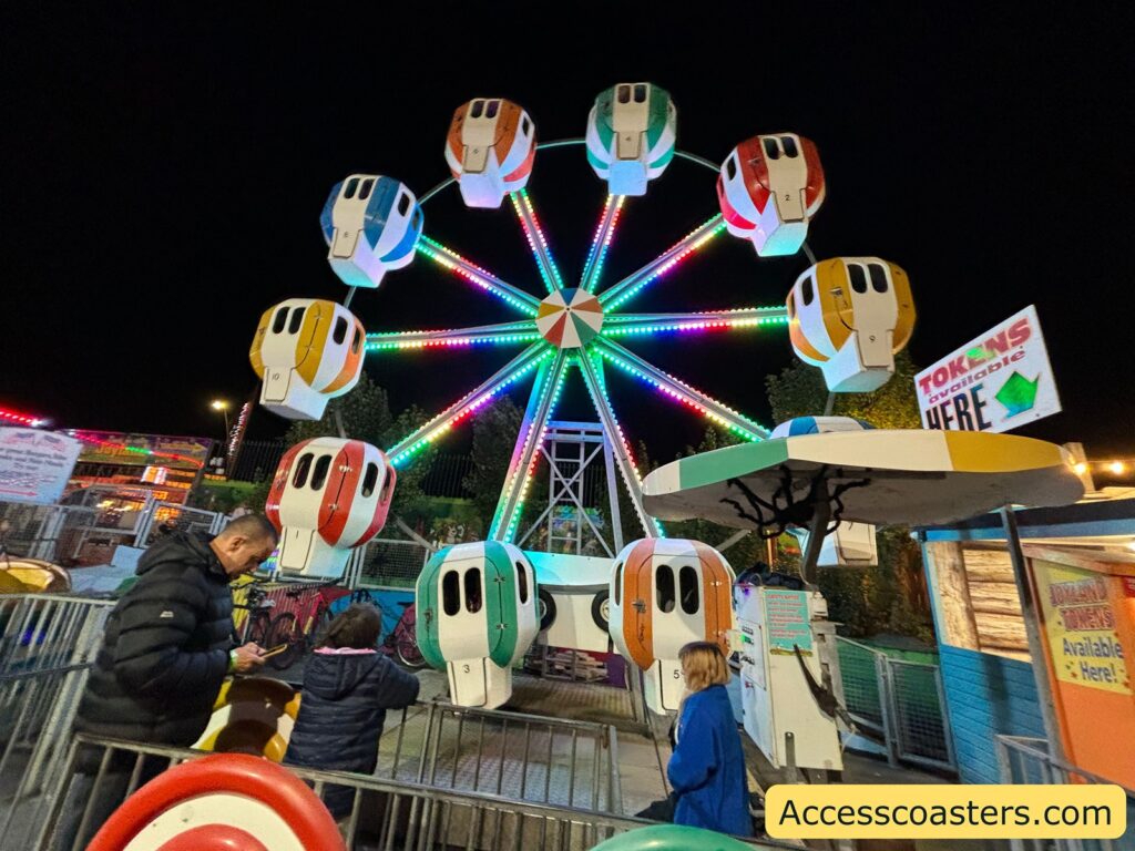 Small Ferris wheel lit up with multi-colored lights at night — caption: Balloon Wheel
