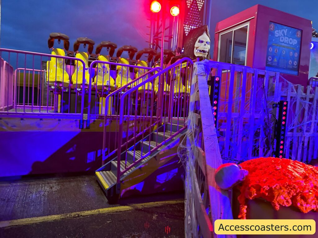 The Sky Drop boarding area from the side, featuring the stairs, handrail, and riders seated with over-the-shoulder restraints.