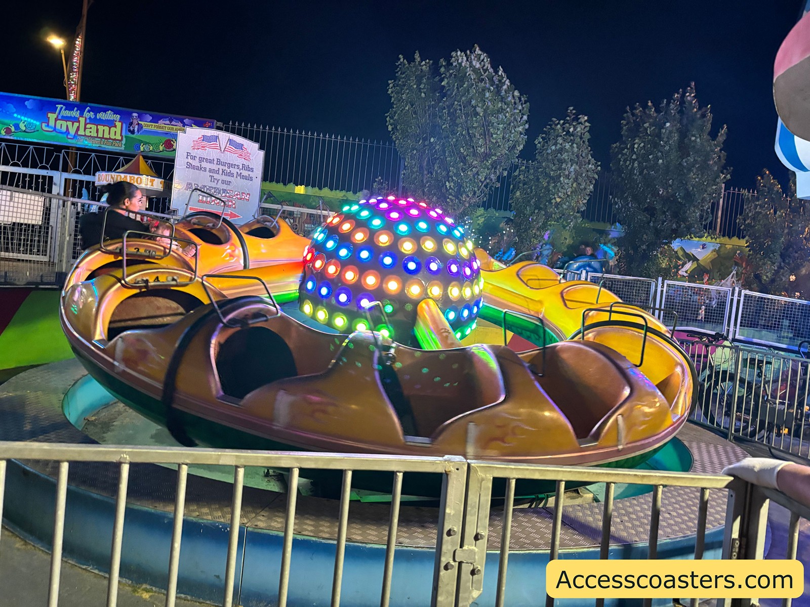 Circular spinning ride with lit center pieces, surrounded by a fence — caption: Major Orbit