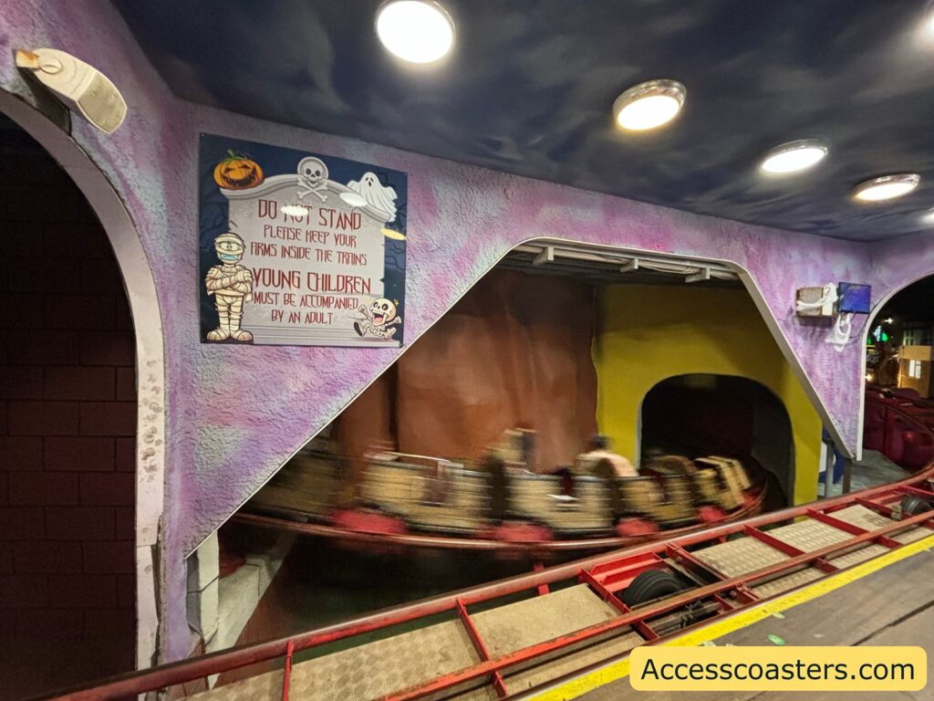 Blurry action view of the Spooky Express rollercoaster moving quickly through a themed section of the ride, inside an indoor area.