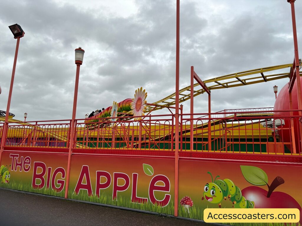 Big Apple roller coaster track with bright yellow rails, and a large sign featuring apple illustrations in front of the ride.