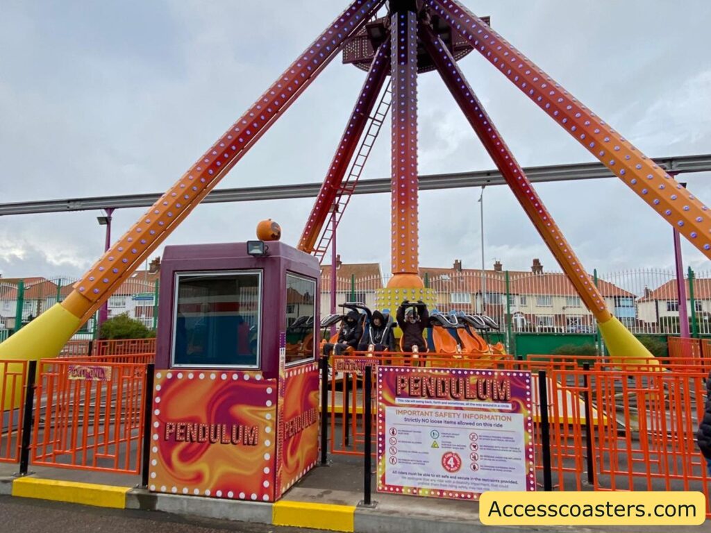 shot of the Pendulum amusement park ride showing its large swinging arm, colorful support beams, and circular seating area. The ride is at the station platform, surrounded by safety barriers, 