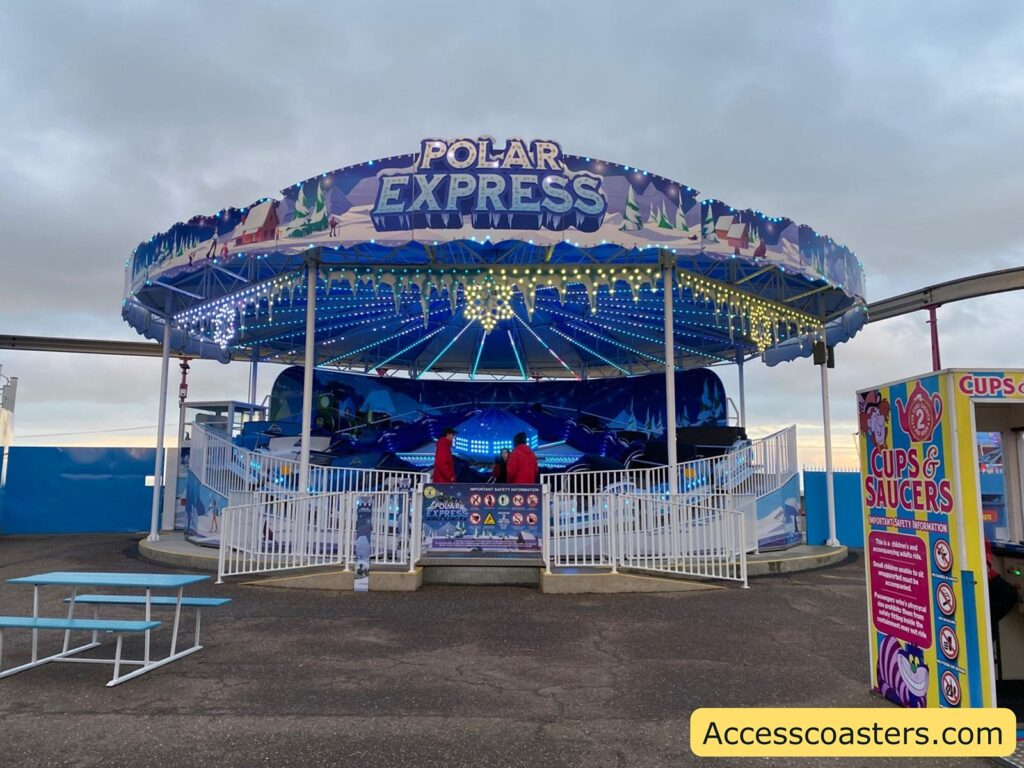 Front view of the Polar Express flat ride, showing the circular ride with a colorful canopy, fenced entrance area, and the name sign above the ride