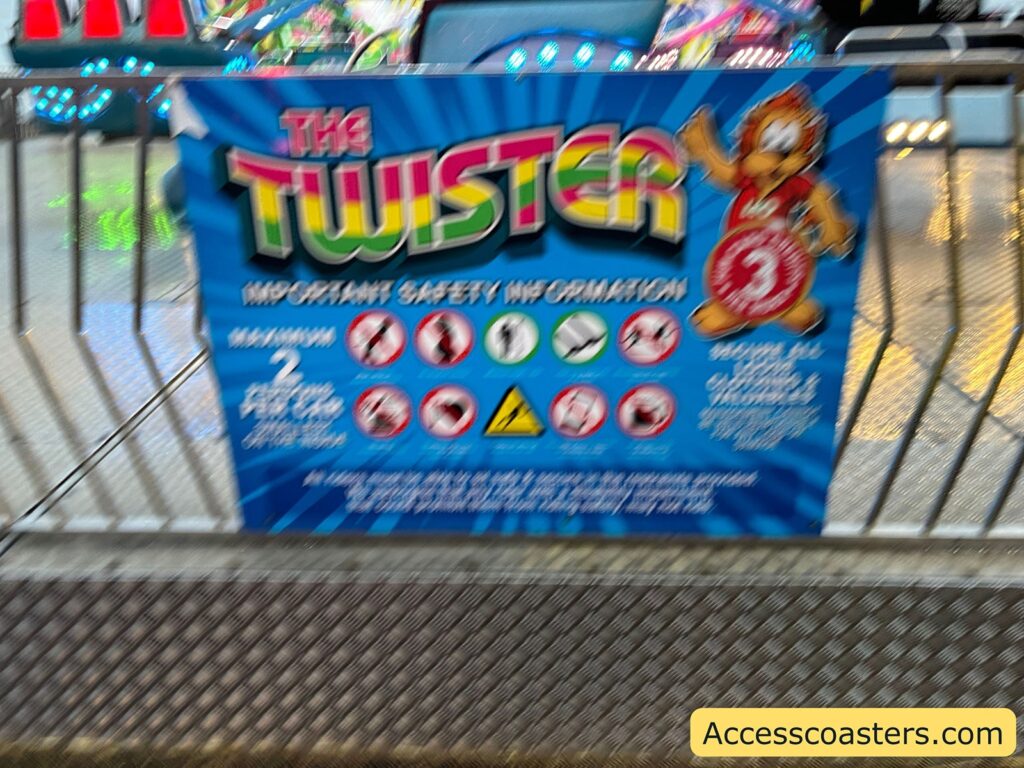 Twister ride safety information sign with colorful graphics, attached to a metal barrier at a fairground. The sign displays important safety details for riders.
