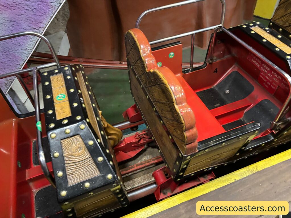 Close-up of a red rollercoaster cart used on the Spooky Express, showing seating and the track mechanism.