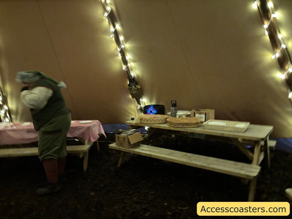 The inside of a festive tent with strings of lights and picnic benches, where people are preparing for a gingerbread decorating session.
