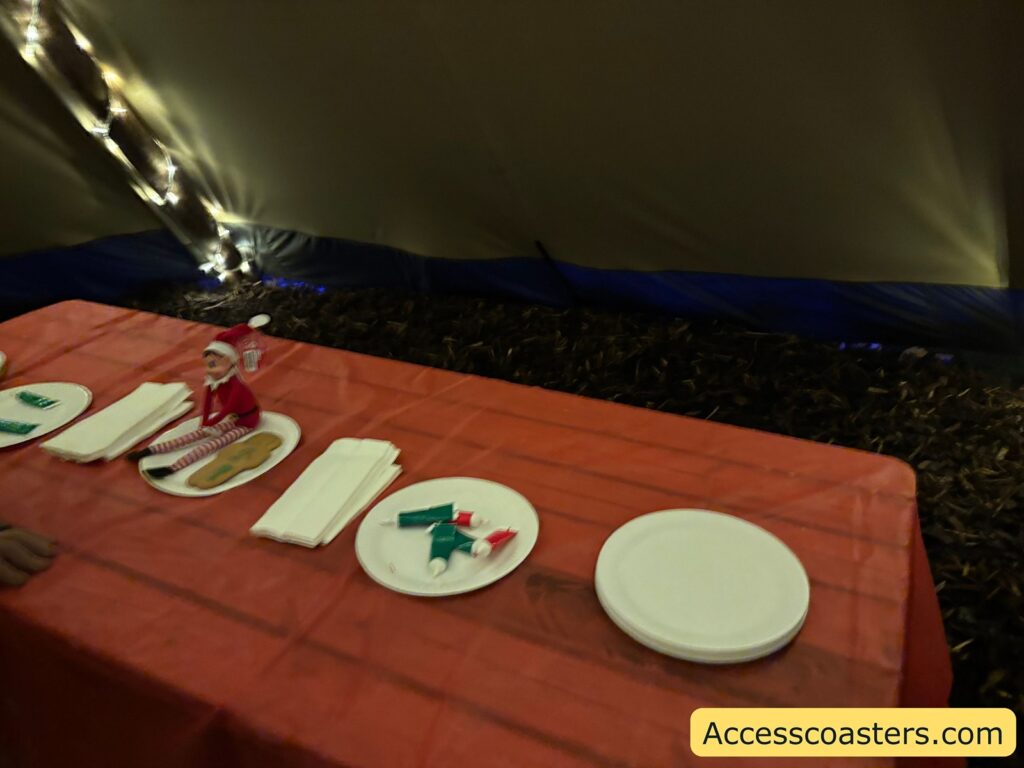 A close-up of a picnic table inside a tent, set with white plates, icing tubes, and gingerbread-shaped decorations ready for a gingerbread decorating activity.