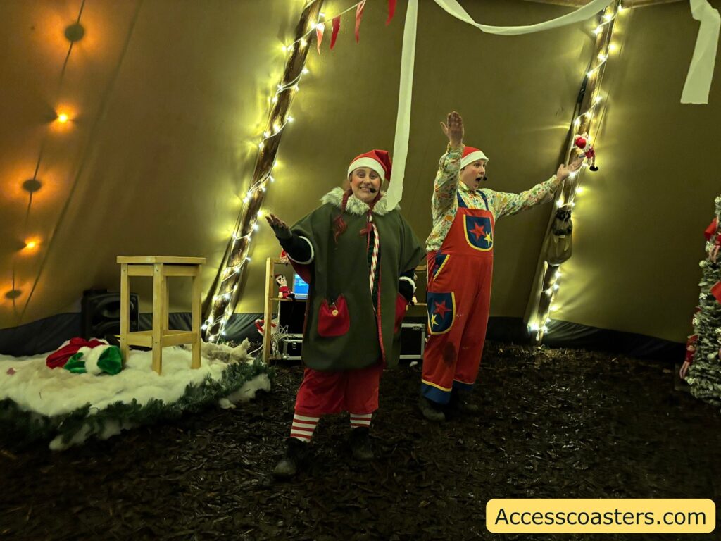 Two elves in colorful costumes posing cheerfully inside the decorated pranking tent, ready to lead the interactive activities.
