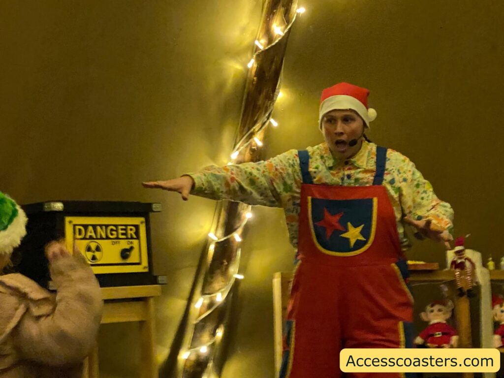 An elf in costume, standing inside the tent, presenting in front of a "DANGER" sign as part of the pranking show.