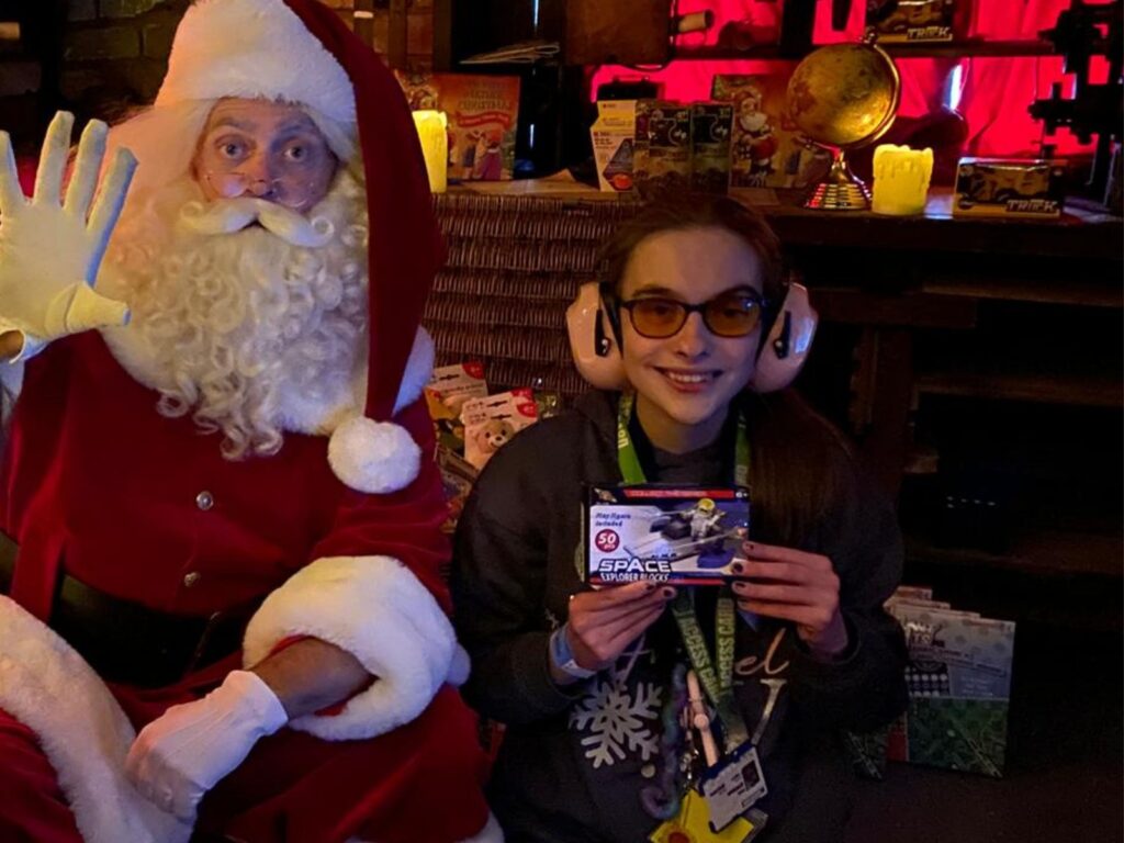 Iona meeting Santa Claus, both smiling at the camera, Iona is holding a present.