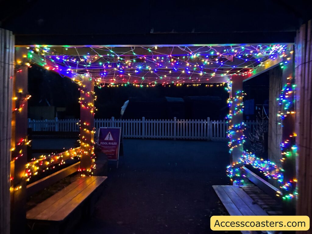 Wooden shelter with benches, brightly decorated with multicolored Christmas string lights.
