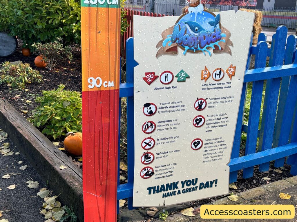 Sign with ride restrictions and information for the Moby Dick ride, featuring a cartoon whale illustration next to a blue fence.