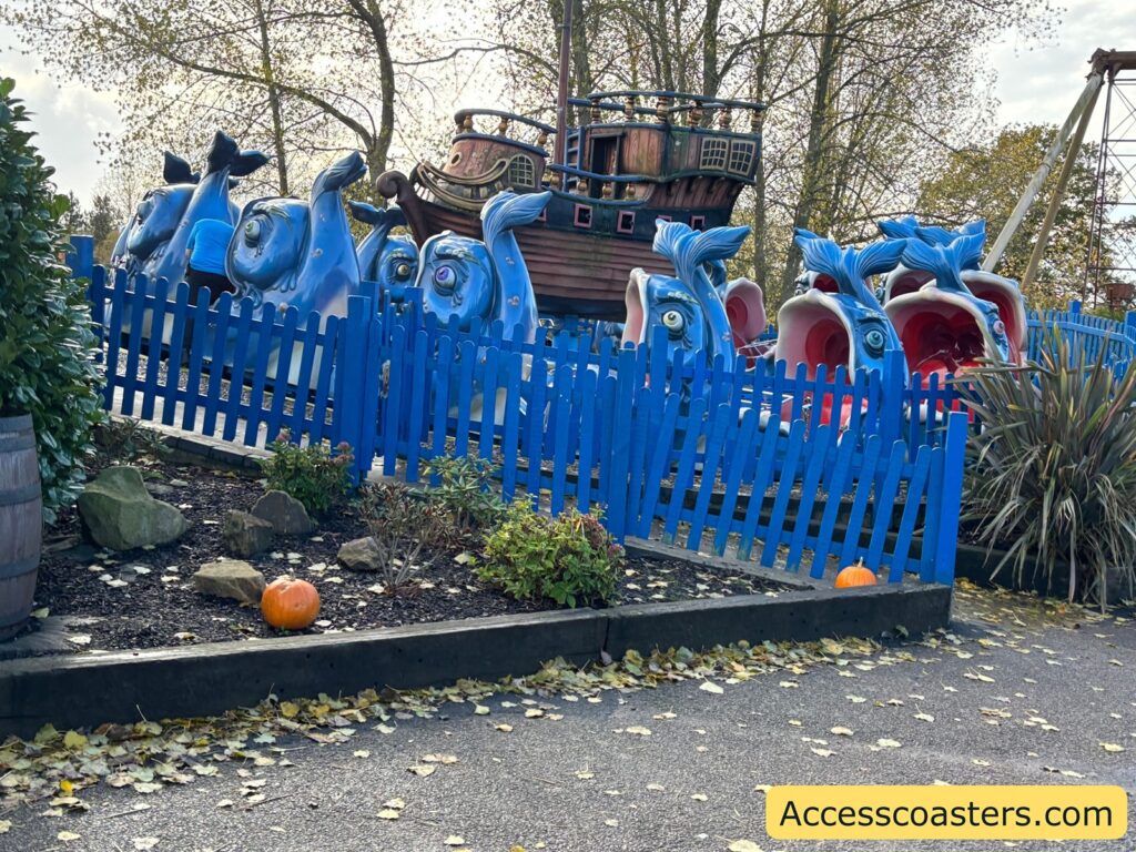 View of the Moby Dick ride showing multiple blue whale-shaped ride carts on a circular track, enclosed by a blue picket fence.