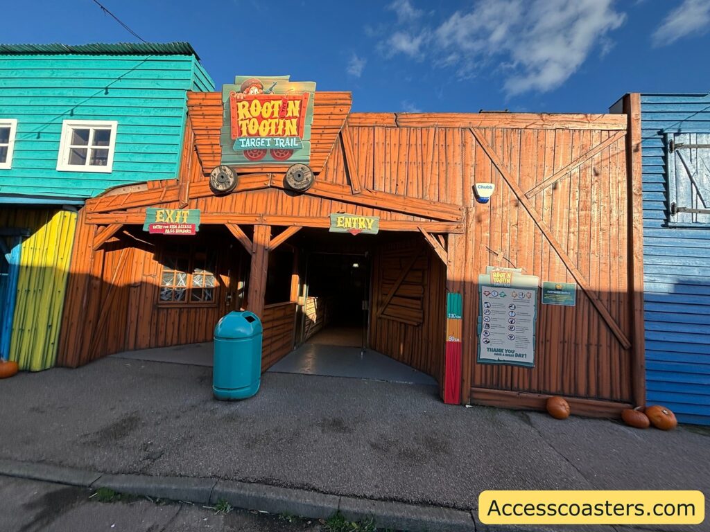The Root N Tootin Target Trail entrance with a wooden wild west theme, including blue and brown buildings and a ride sign above the entryway.