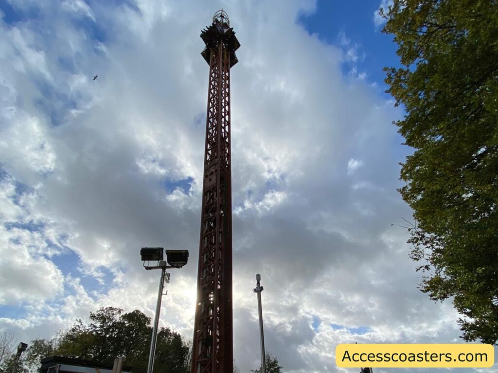 View looking up at the tall, vertical Jolly Roger drop tower, with clouds and trees in the background.