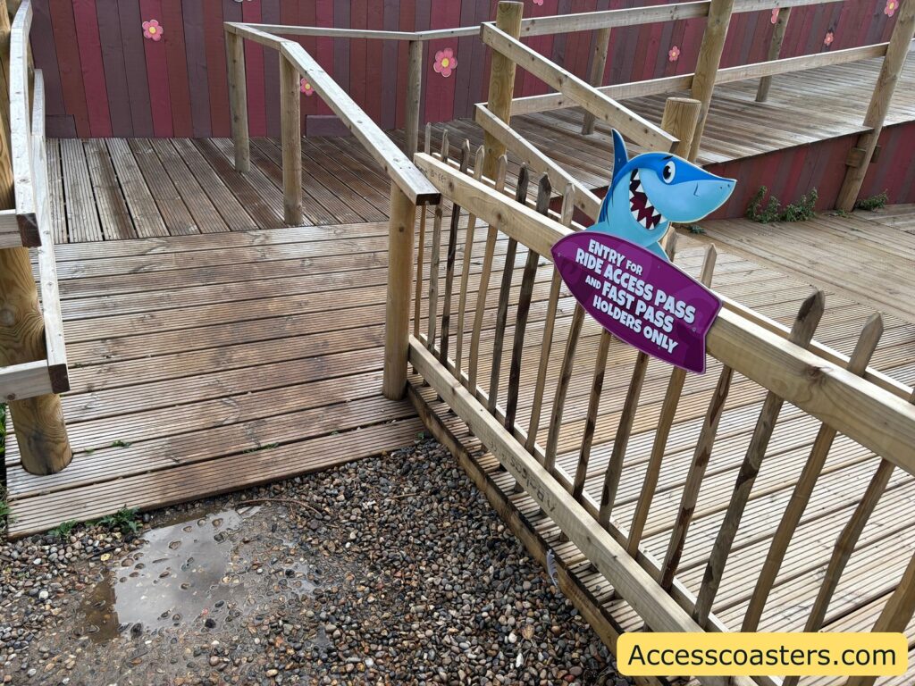 A wooden ramp with handrails and a sign for the designated ride access pass entrance, next to the Wipeout ride station.