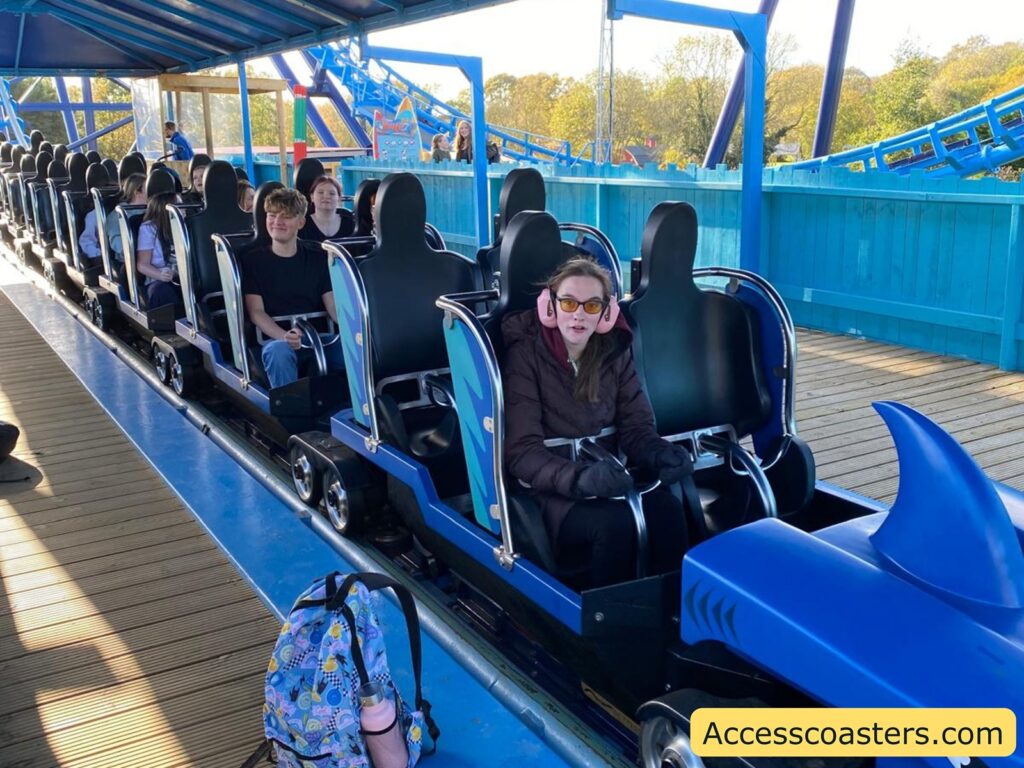The interior of the Wipeout roller coaster station with riders seated in the blue coaster train, ready for departure.