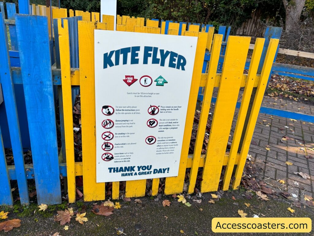 Sign for the "Kite Flyer" ride attached to a colorful wooden fence, displaying ride instructions and safety information.