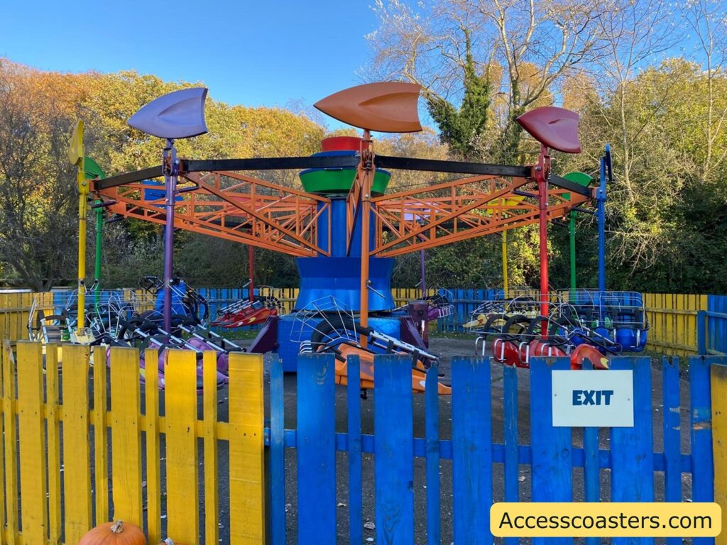 Closer view of the Kite Flyer ride and its exit area, featuring labeled “Exit” signs and the colorful fencing around the attraction.