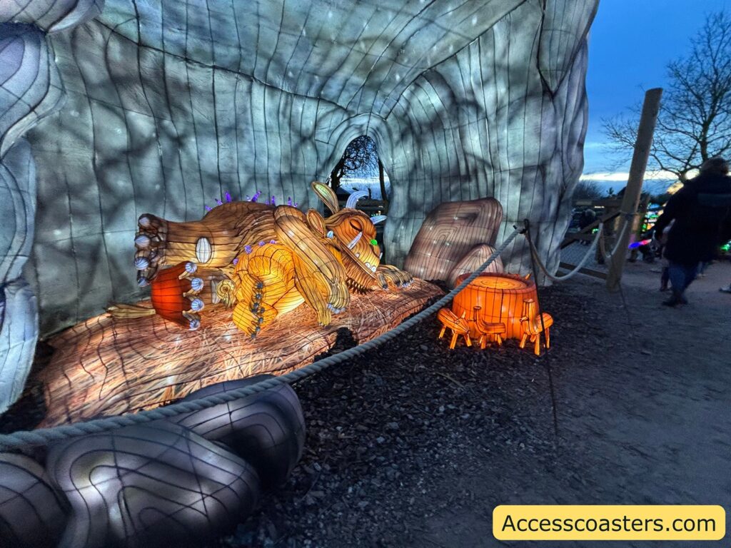 illuminated figure of the Gruffalo resting beside a den-like structure on the trail.