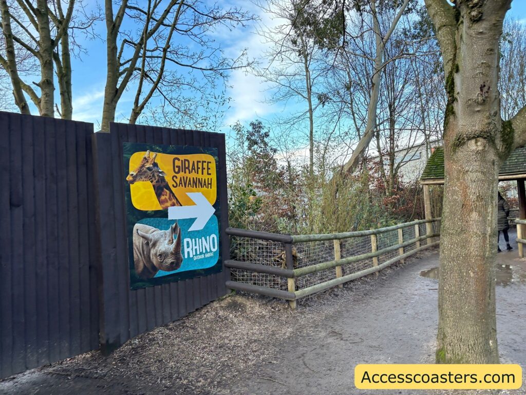Outdoor path leading toward the Giraffe Savannah and Rhino area, with a sign on a dark fence.
