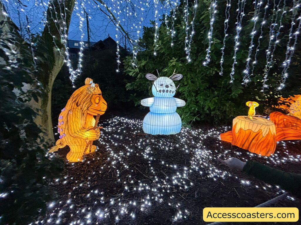 Light display with a Gruffalo figure, a snowman, and the mouse under hanging white lights in the trees.
