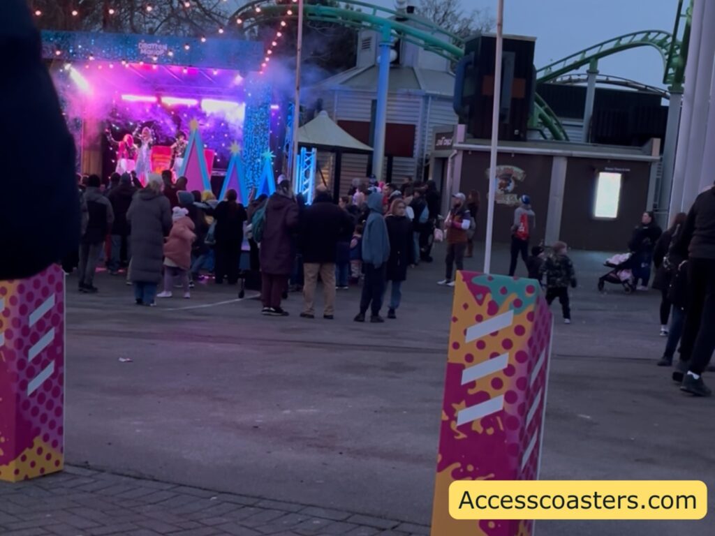 Crowd gathered in front of the main stage during the K-pop end-of-day concert, with bright purple and blue stage lighting and people standing to watch.