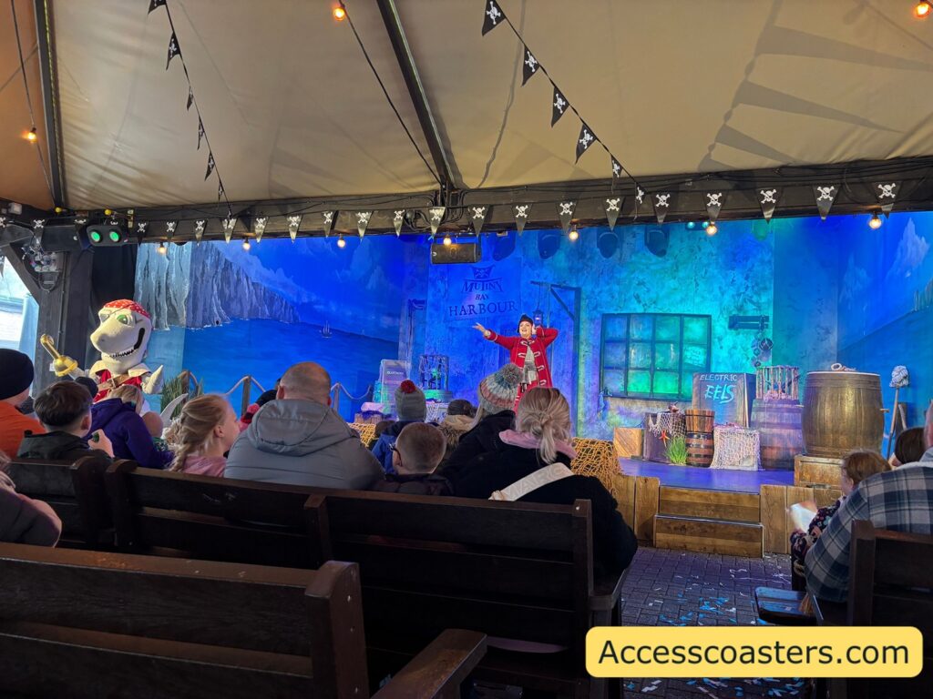 Wide shot of the Captain Finn’s Training Camp stage show inside a big tent, with blue lighting and a seated audience in the foreground.