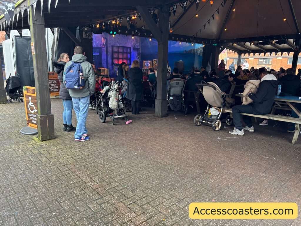 View into the courtyard theatre accessible viewing area and seating area under a canopy, with benches and people gathering and watching.