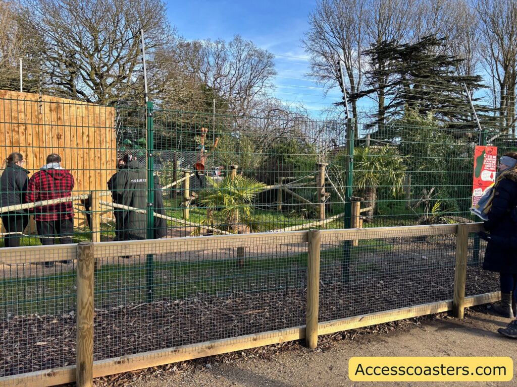 Fenced outdoor animal enclosure with a small wooden shelter and trees.
