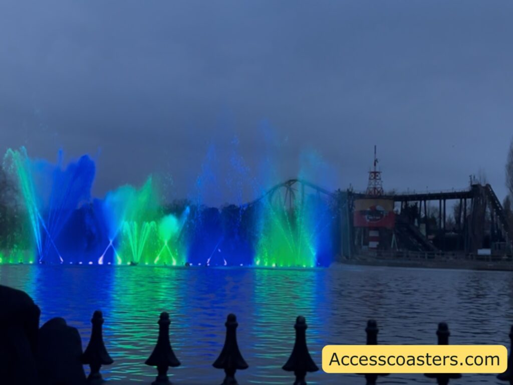 Water fountains glowing blue and green across the lake during the show, with reflections on the water.
