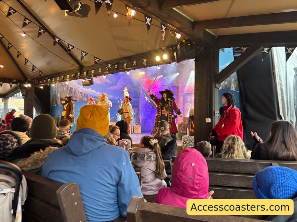 Indoor courtyard theatre audience watching Pirates of Mutiny Bay: The Haunt for the Crown of T’Hulu, with pirates singing and dancing onstage under purple lighting.