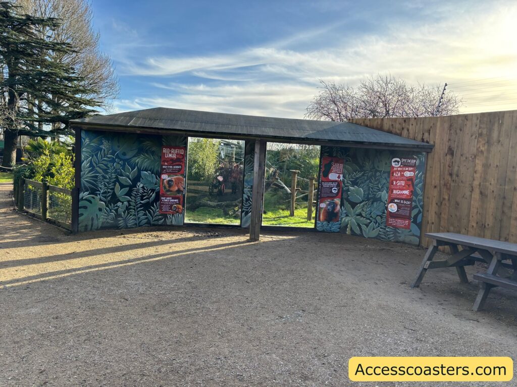 Covered zoo shelter area for birds with benches beside a wide paved space.
