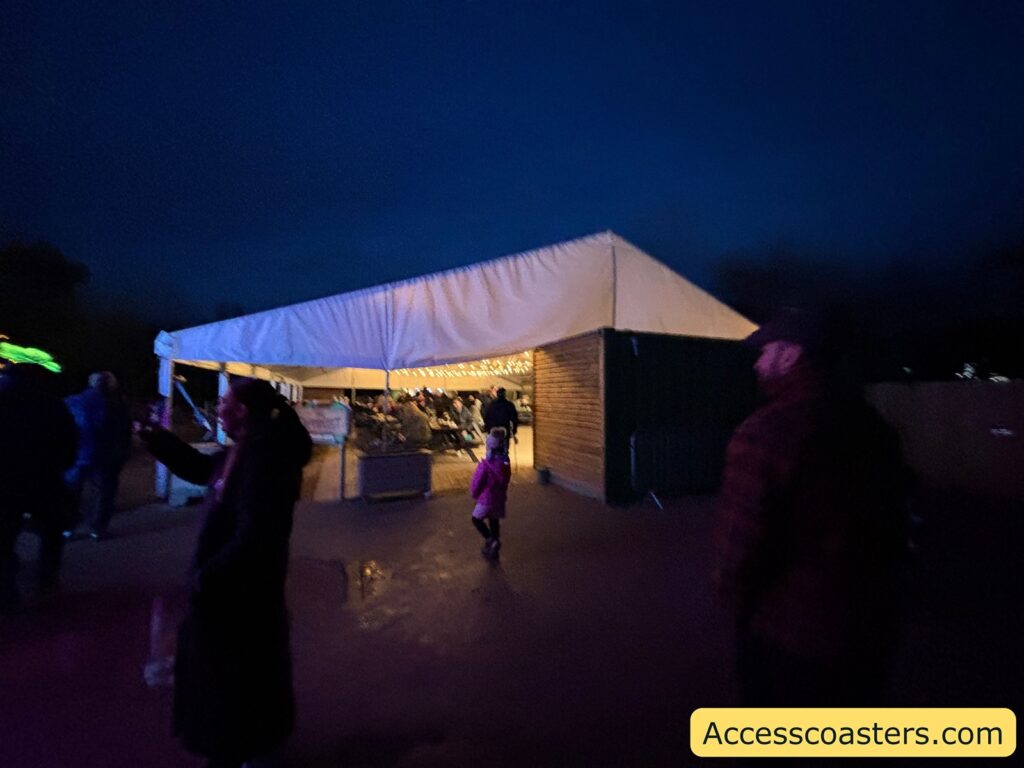 marquee tent at the light trail, lit from inside, with people walking past on the wet ground.