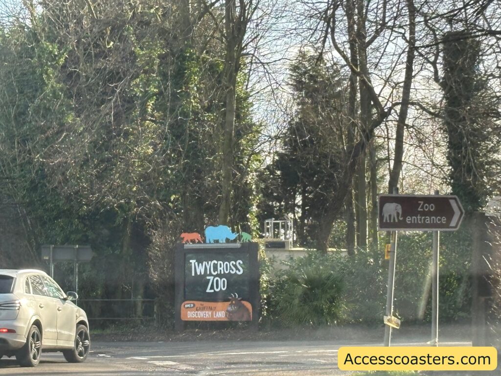 Outdoor view of the Twycross Zoo entrance area with trees and a Twycross Zoo sign in the foreground.
