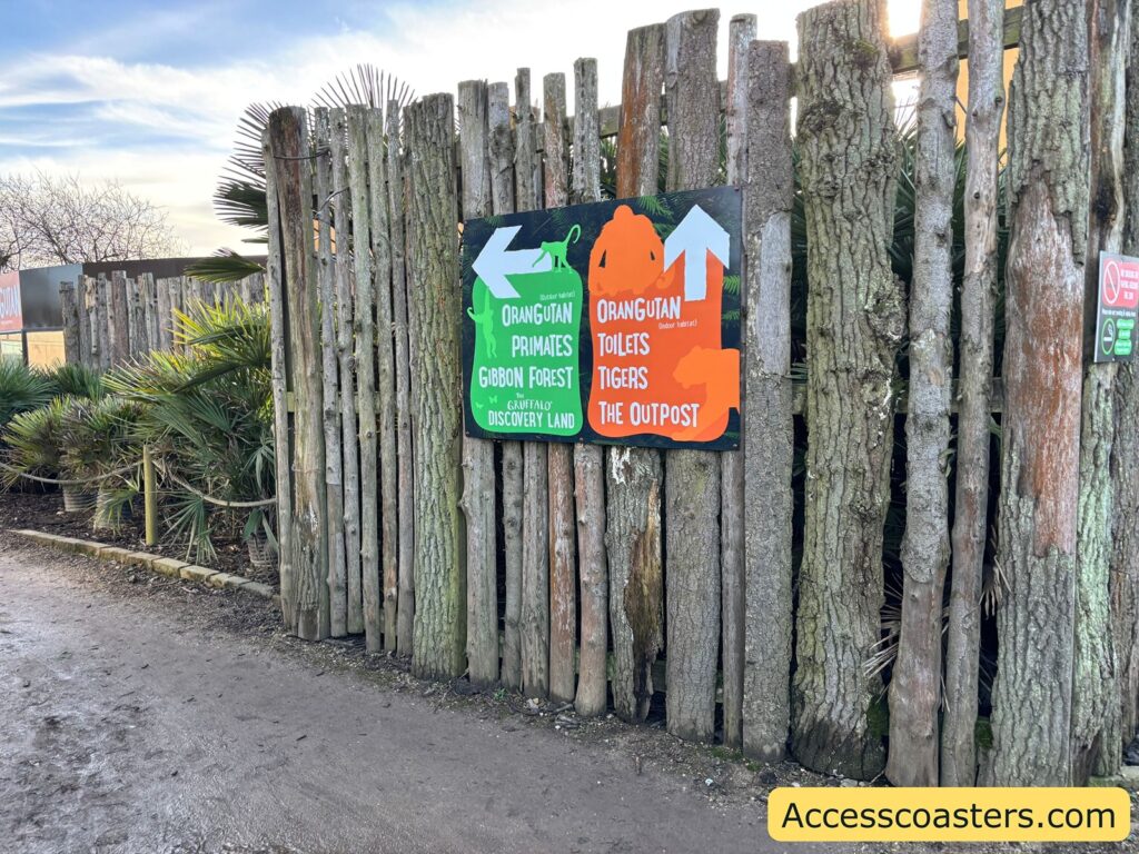 Rustic wooden fence and entrance area with a bright green-and-orange sign for the Gruffalo trail.
