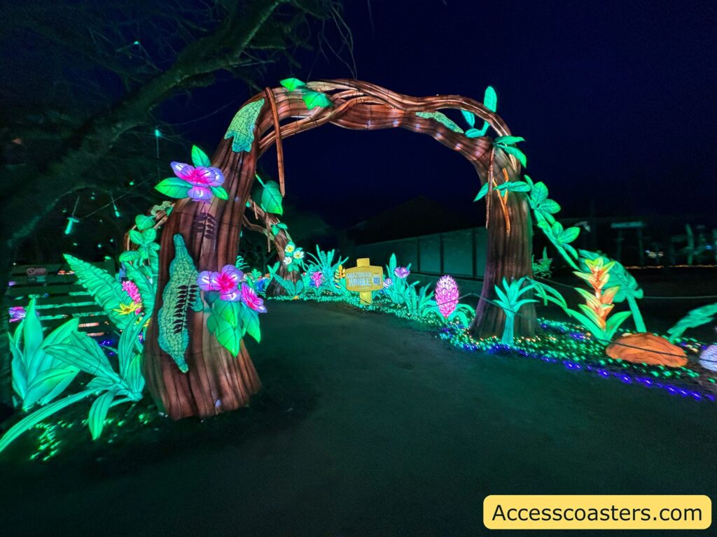 Neon-lit jungle trail with a tree-and-vine archway over a paved, wheelchair-accessible path at night.