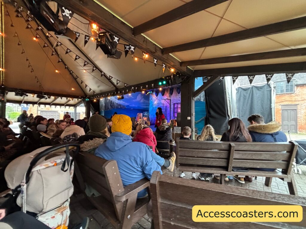 Crowded bench seating under the canopy, with people seated and facing the stage area with purple/blue lighting.