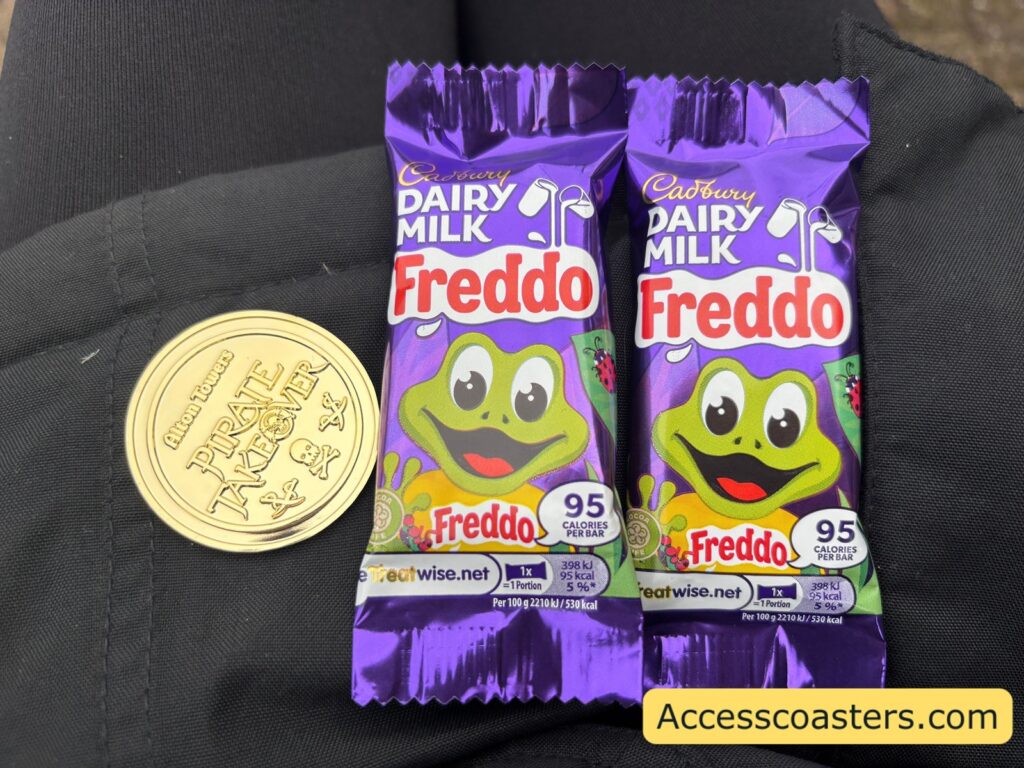 Image of a small golden coin with the pirate takeover logo on and 2 choclate fredo's