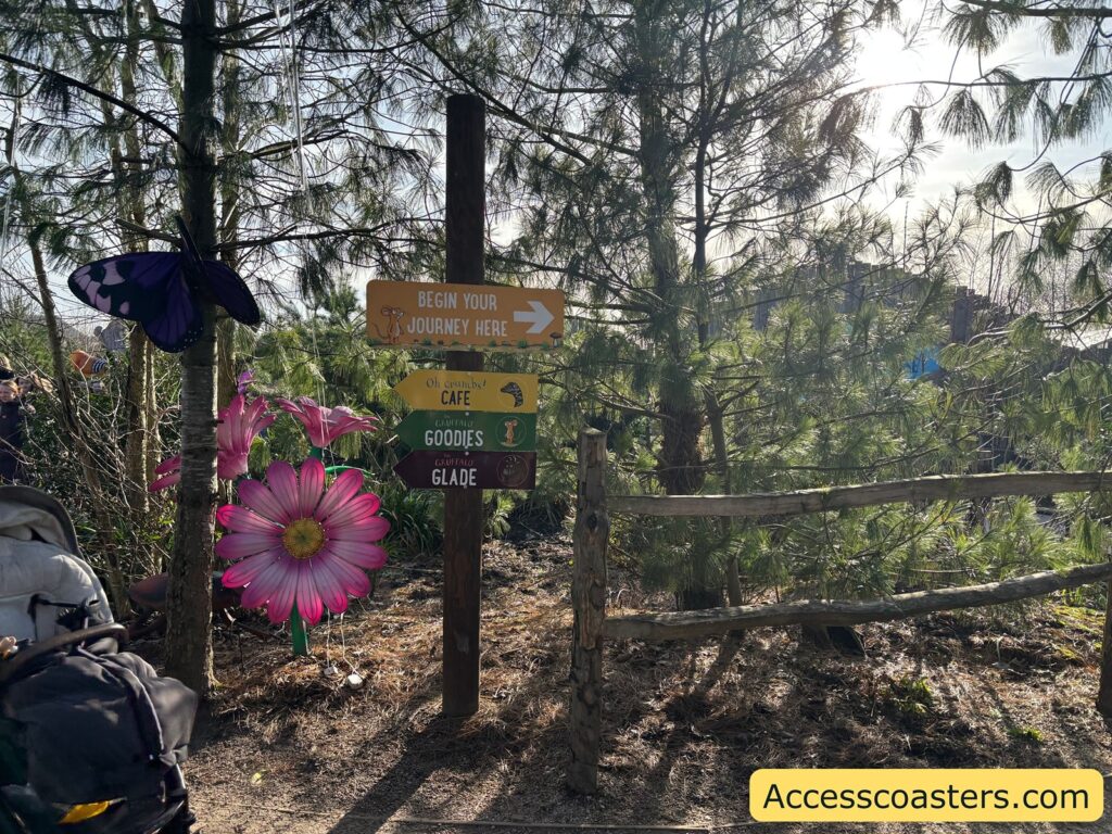 Woodland trail junction with multiple direction signs and a large pink flower decoration.
