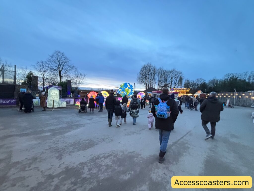 Wide walkway at dusk with crowds moving toward the Lanterns event area and lights ahead in the distance.