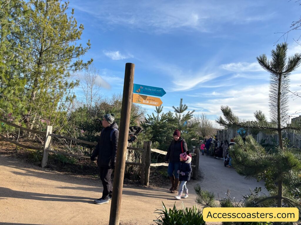 Trail path with visitors walking toward wooden signposts among trees and shrubs.

