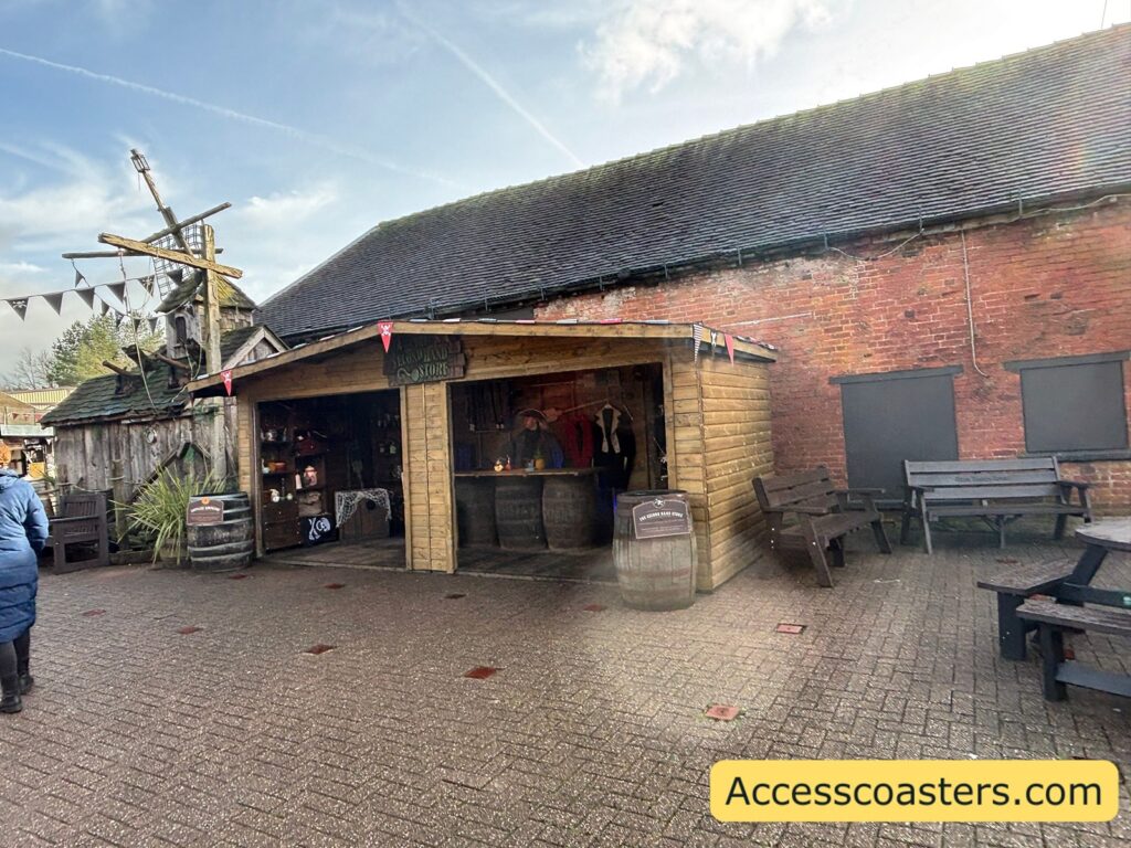 A wider view of rustic buildings (brick and wood) with barrels and benches outside.