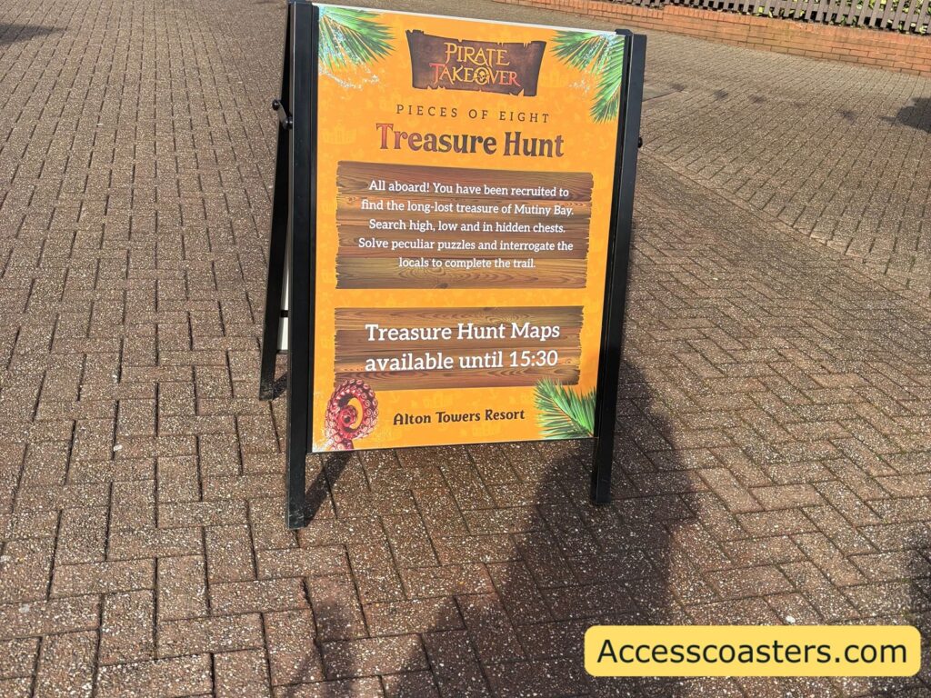 A freestanding A-frame sign on a brick-paved walkway. The sign has a pirate-themed background and large text that includes “Treasure Hunt.” and an explanation how to join in